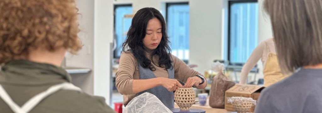 An artist builds a woven ceramic vessel by hand while others watch